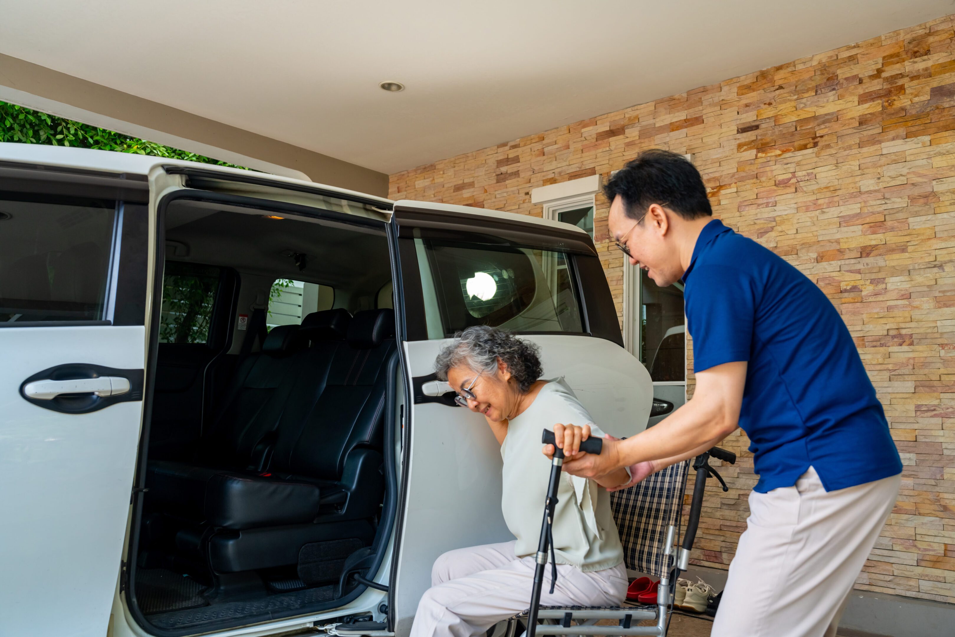Asian man caregiver or taxi driver helping senior woman patient get in the car to get to medical appointments or healthcare therapy sessions at hospital. Assisted elderly patient transportation services Asian man caregiver or taxi driver helping senior woman patient get in the car to get to medical appointments or healthcare therapy sessions at hospital. Assisted elderly patient transportation services