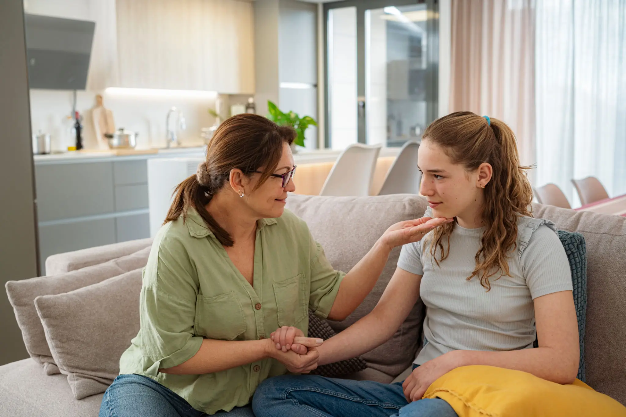 Mother comforting daughter on living room couch.