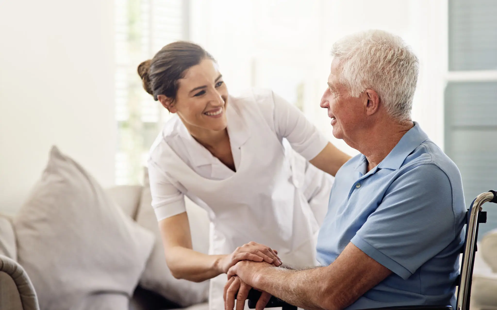 Caregiver smiling with elderly man in wheelchair.