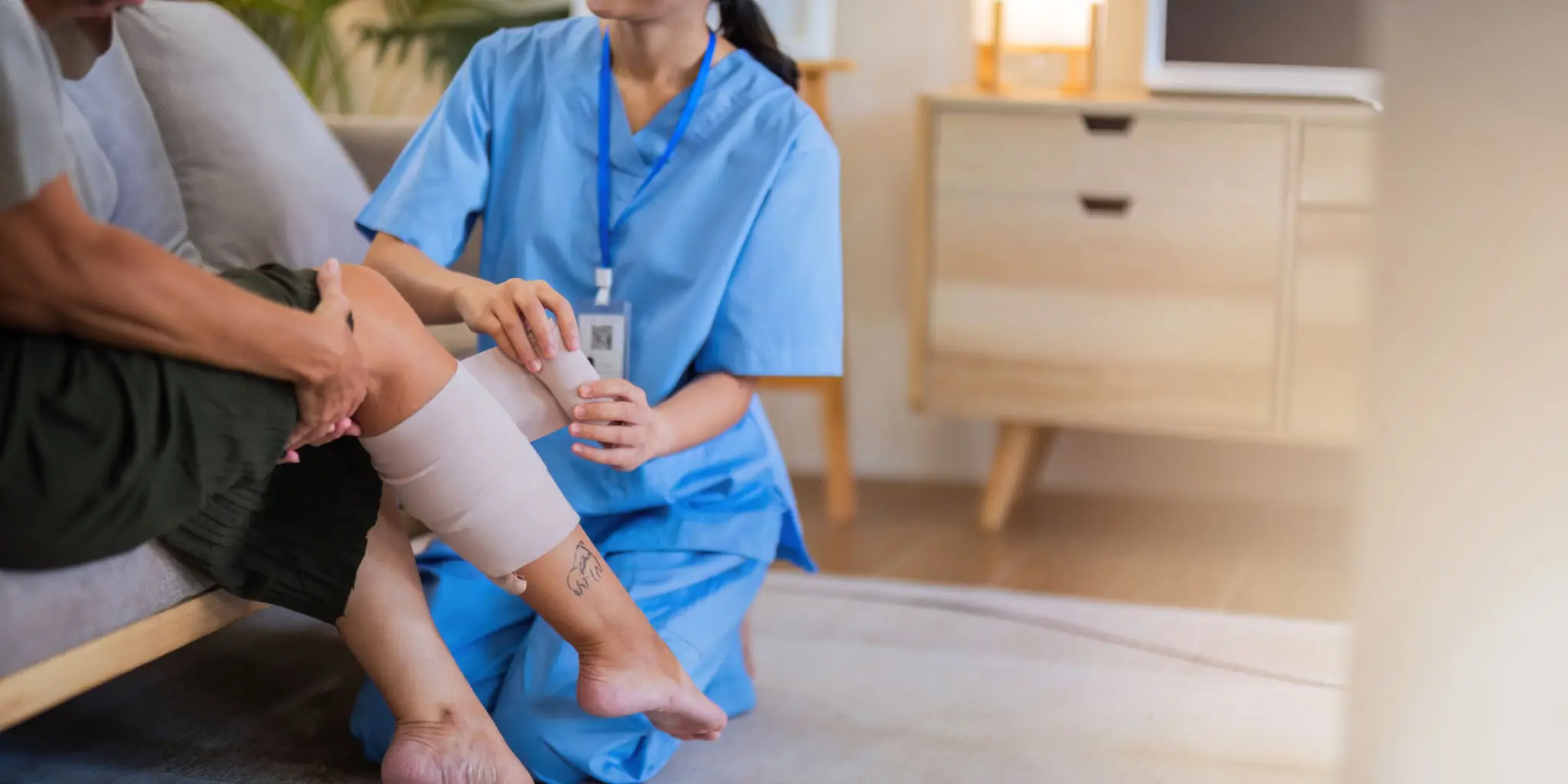 Nurse bandaging patient's leg in home setting.
