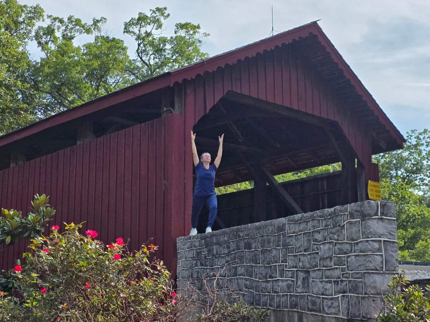 Person standing on stone wall by bridge.