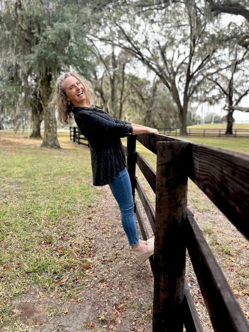 Woman playfully leaning on wooden fence outdoors.
