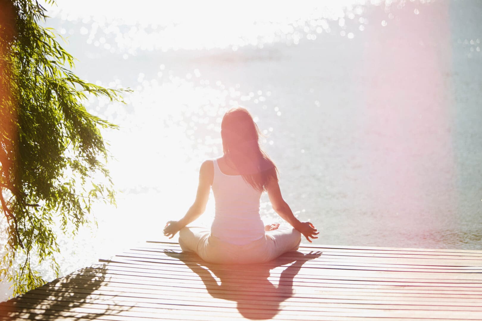 Woman meditating on a sunlit dock.