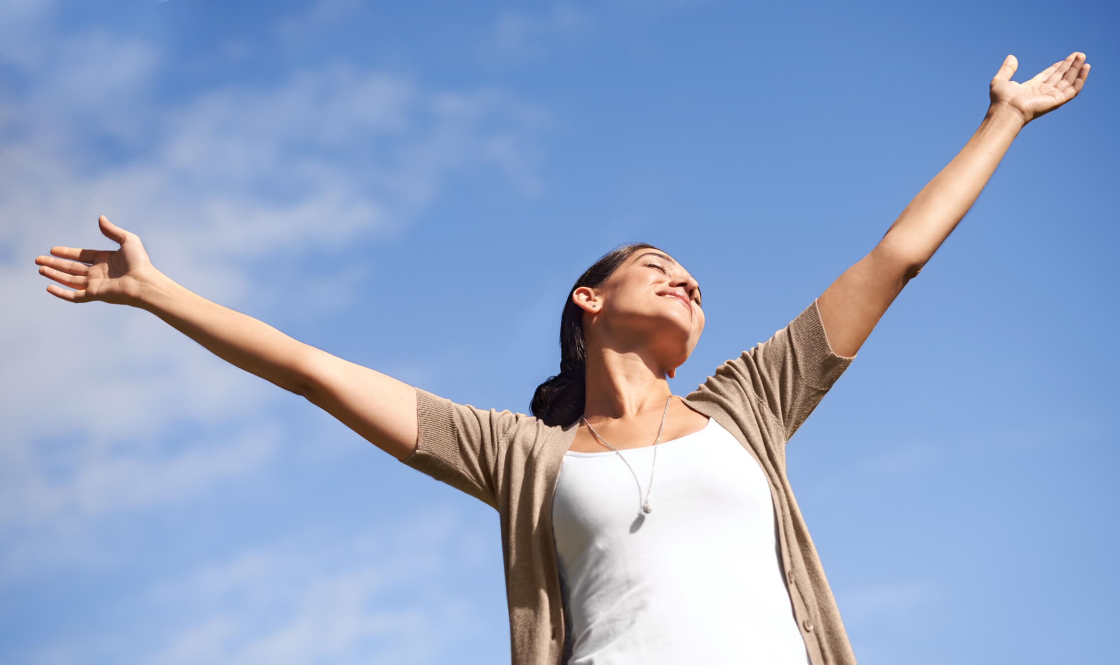 Woman joyfully stretching arms under blue sky.
